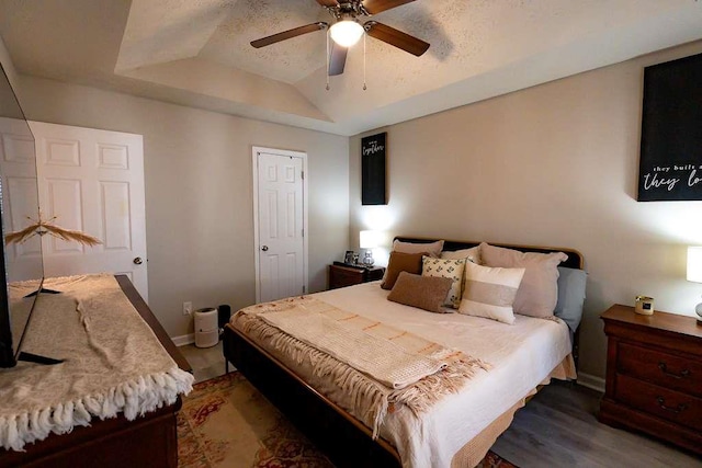 bedroom with a raised ceiling, dark hardwood / wood-style floors, and ceiling fan