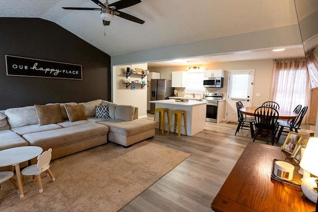 living room with ceiling fan, lofted ceiling, and light wood-type flooring