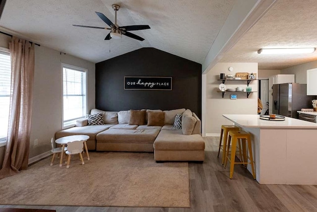 living room featuring lofted ceiling, ceiling fan, light hardwood / wood-style floors, and a textured ceiling