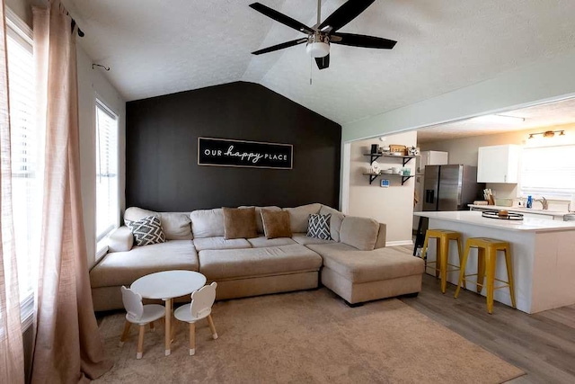 living room featuring vaulted ceiling, a healthy amount of sunlight, ceiling fan, and light wood-type flooring