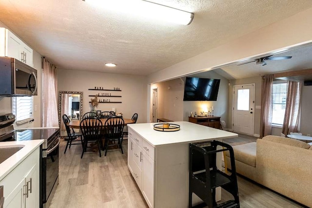 kitchen with stainless steel appliances, a center island, white cabinets, and light hardwood / wood-style floors