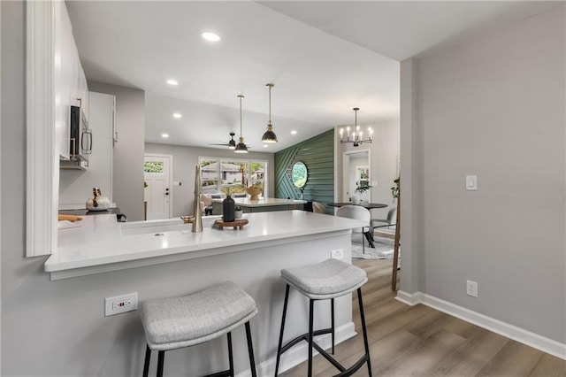 kitchen featuring a peninsula, a kitchen bar, stainless steel microwave, white cabinets, and dark wood finished floors
