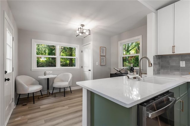 kitchen featuring decorative backsplash, light wood-type flooring, dishwasher, a sink, and baseboards
