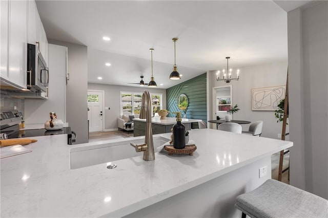 kitchen with a kitchen breakfast bar, a sink, light stone counters, stainless steel appliances, and white cabinetry