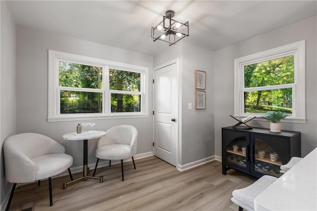 living area featuring baseboards, a chandelier, a healthy amount of sunlight, and light wood-style flooring
