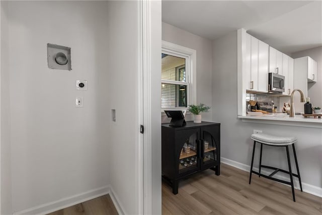 kitchen with a kitchen breakfast bar, white cabinetry, stainless steel microwave, light countertops, and light wood-style floors
