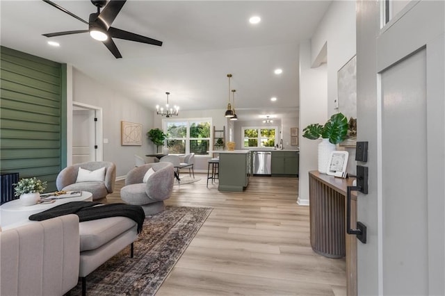 living area with baseboards, ceiling fan with notable chandelier, lofted ceiling, recessed lighting, and light wood-style flooring