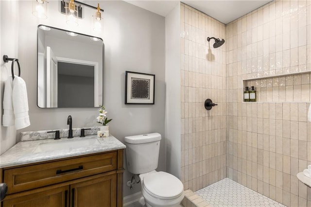 bathroom with toilet, a tile shower, and vanity