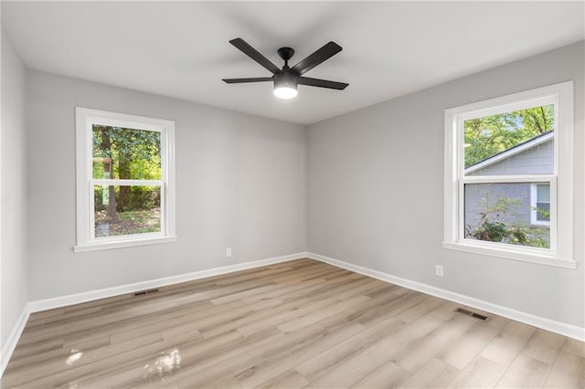empty room with light wood finished floors, visible vents, and baseboards