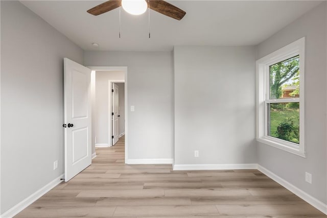 spare room featuring light wood-type flooring, a ceiling fan, and baseboards