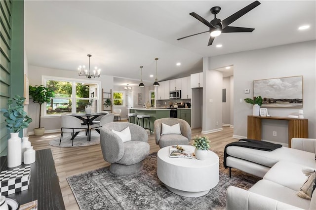 living area with light wood-style floors, ceiling fan with notable chandelier, recessed lighting, baseboards, and vaulted ceiling
