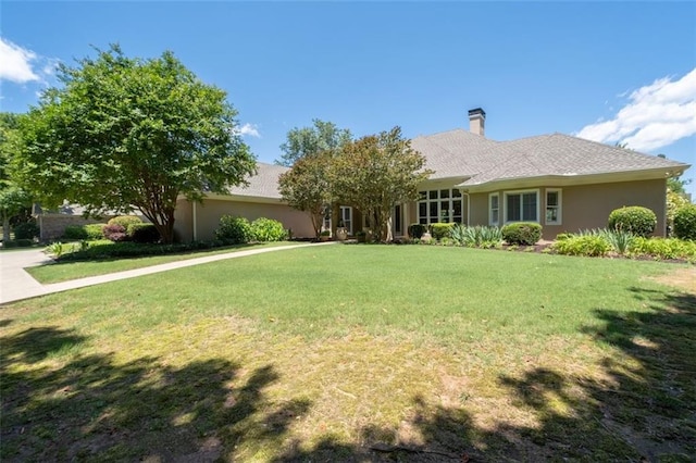 ranch-style house featuring a chimney, a front yard, and stucco siding