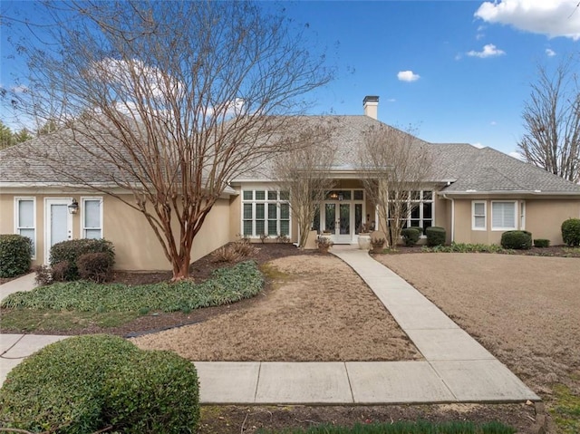 view of front of house featuring french doors, roof with shingles, a chimney, and stucco siding