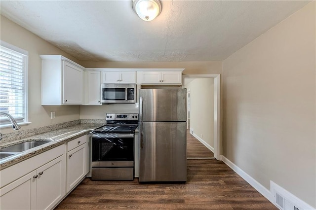 kitchen with sink, white cabinetry, stainless steel appliances, dark hardwood / wood-style floors, and light stone countertops