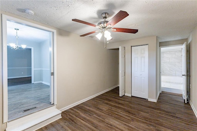 unfurnished bedroom with two closets, dark wood-type flooring, ceiling fan with notable chandelier, and a textured ceiling