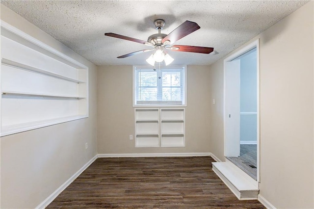 unfurnished room with ceiling fan, built in shelves, dark wood-type flooring, and a textured ceiling