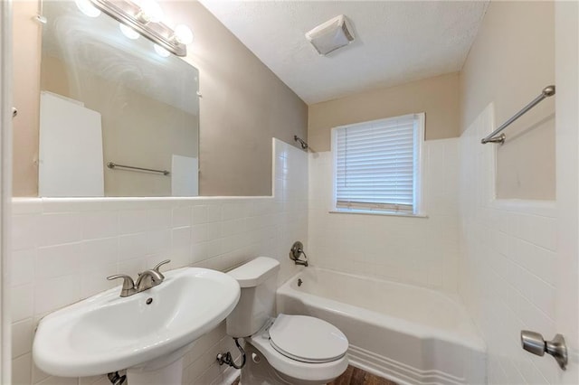 full bathroom featuring tiled shower / bath, toilet, sink, and tile walls