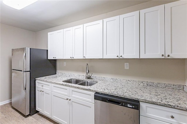 kitchen with sink, light wood-type flooring, appliances with stainless steel finishes, light stone countertops, and white cabinets