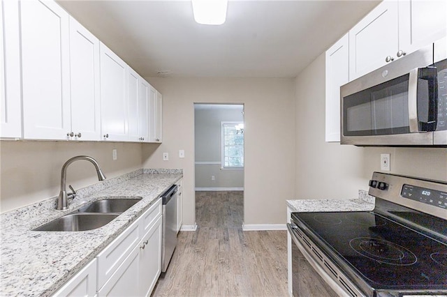 kitchen with sink, appliances with stainless steel finishes, light stone counters, light hardwood / wood-style floors, and white cabinets