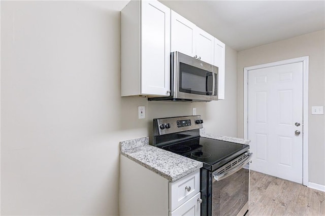 kitchen with stainless steel appliances, light stone counters, white cabinets, and light wood-type flooring