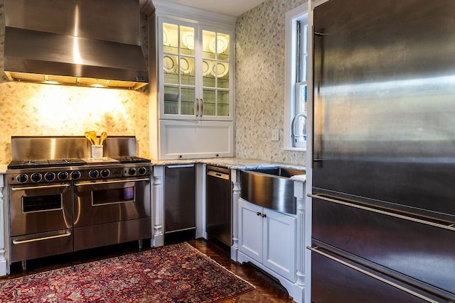 kitchen featuring stainless steel appliances, wall chimney exhaust hood, light stone countertops, and wallpapered walls