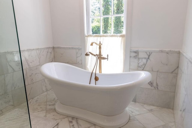 full bathroom featuring marble finish floor, tile walls, a soaking tub, and wainscoting