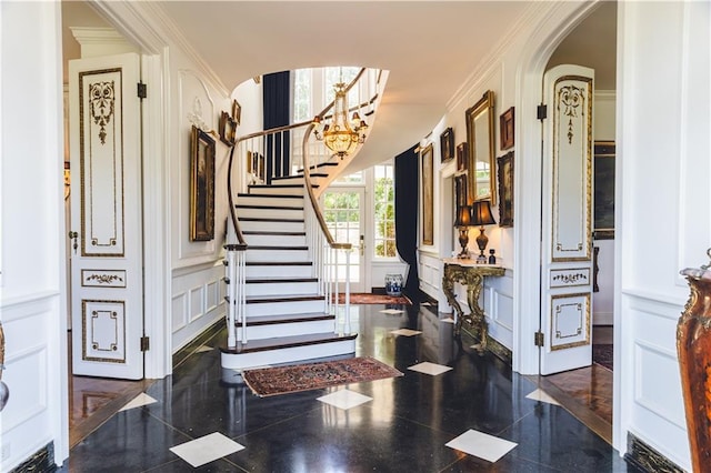 foyer featuring ornamental molding, stairs, a decorative wall, and granite finish floor