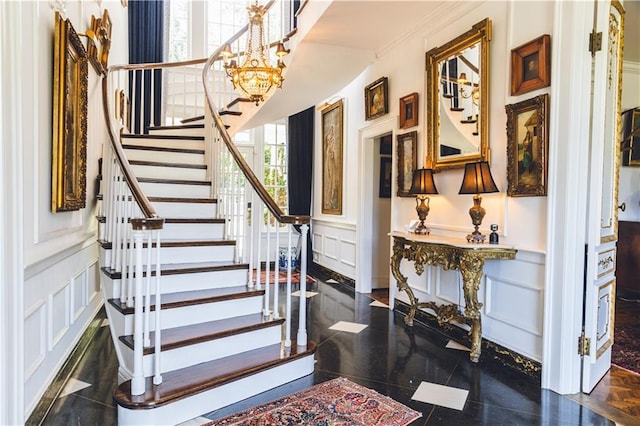 foyer with a wainscoted wall, stairway, an inviting chandelier, and a decorative wall