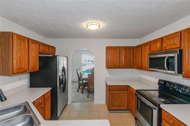 11354 Conner Ct, Hampton, GA 30228 - kitchen featuring stainless steel appliances, arched walkways, light flooring, light countertops, and brown cabinetry