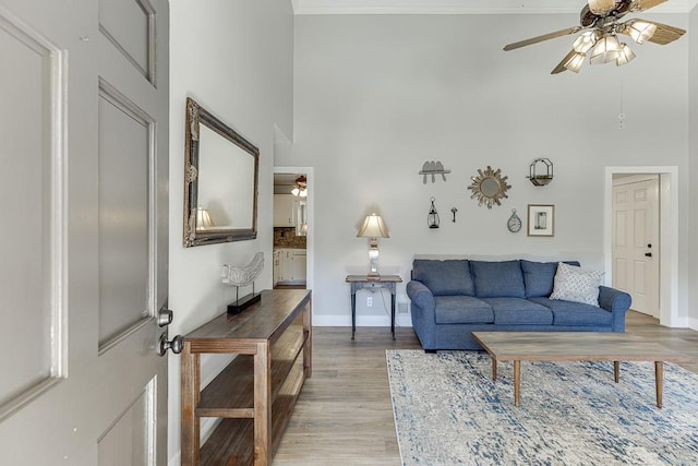 living room featuring a ceiling fan, light wood-type flooring, ornamental molding, and a high ceiling