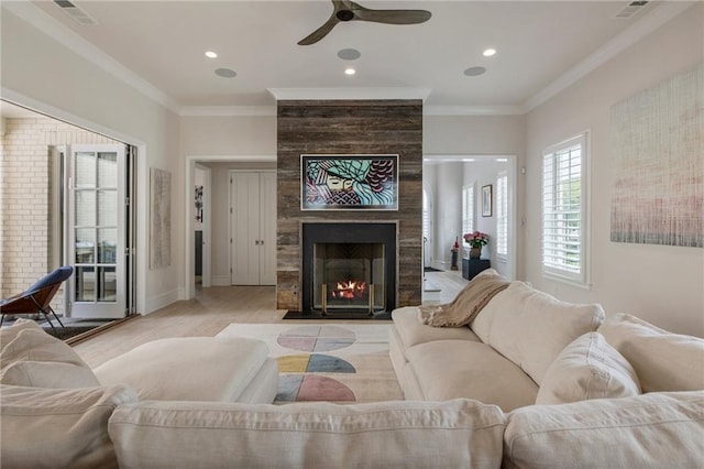 living room with ornamental molding, a ceiling fan, light wood-type flooring, and a tile fireplace