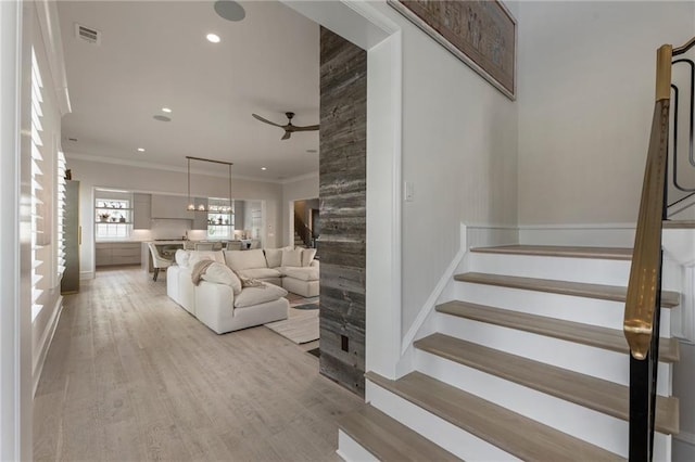 stairway with ornamental molding, a ceiling fan, wood finished floors, and visible vents