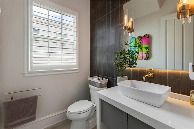 half bathroom with vanity, decorative backsplash, baseboards, and toilet