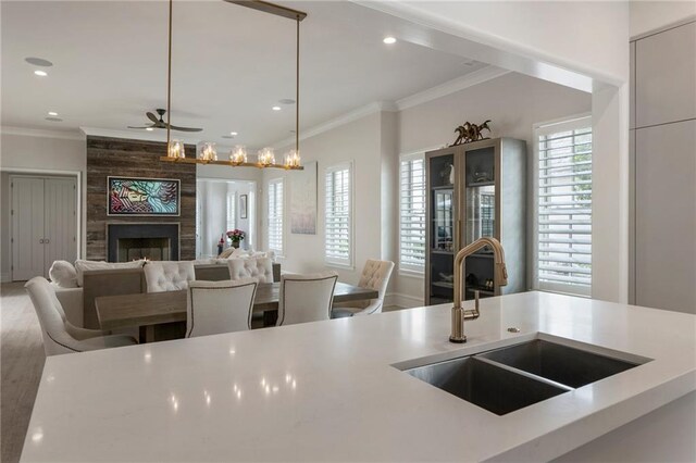 kitchen with a fireplace, open floor plan, ceiling fan, light countertops, and a sink