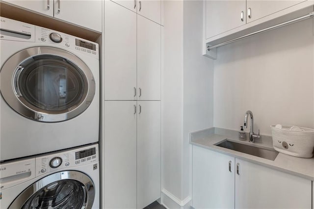 clothes washing area with a sink, stacked washer and clothes dryer, and cabinet space