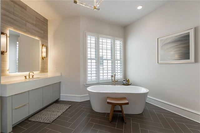bathroom featuring baseboards, a soaking tub, vanity, and recessed lighting