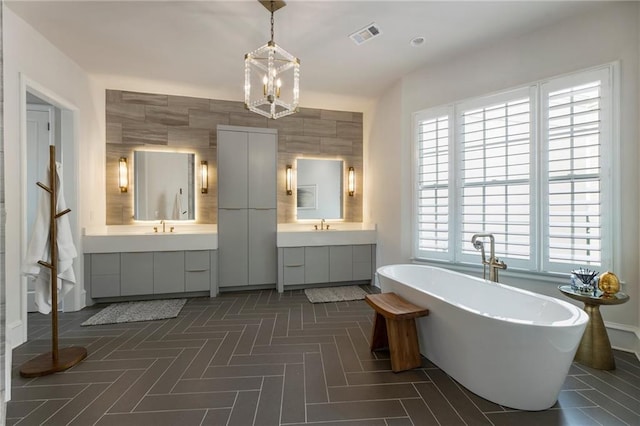 bathroom featuring a freestanding bath, visible vents, two vanities, and a wealth of natural light