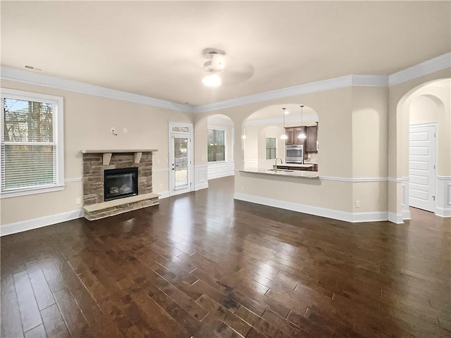 unfurnished living room with a sink, ornamental molding, baseboards, a fireplace, and dark wood-style flooring