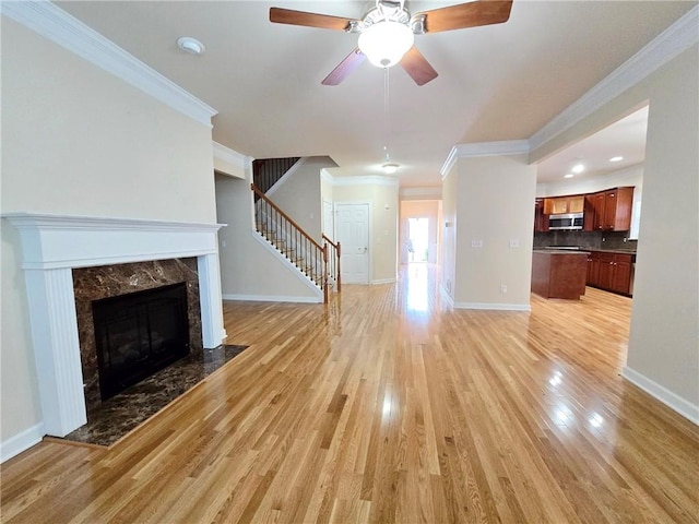 unfurnished living room with stairway, a ceiling fan, light wood finished floors, baseboards, and ornamental molding