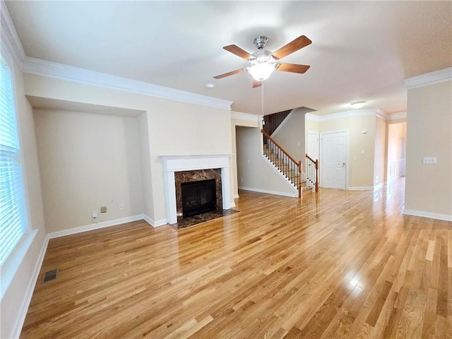 unfurnished living room with stairway, crown molding, ceiling fan, light wood-style flooring, and visible vents