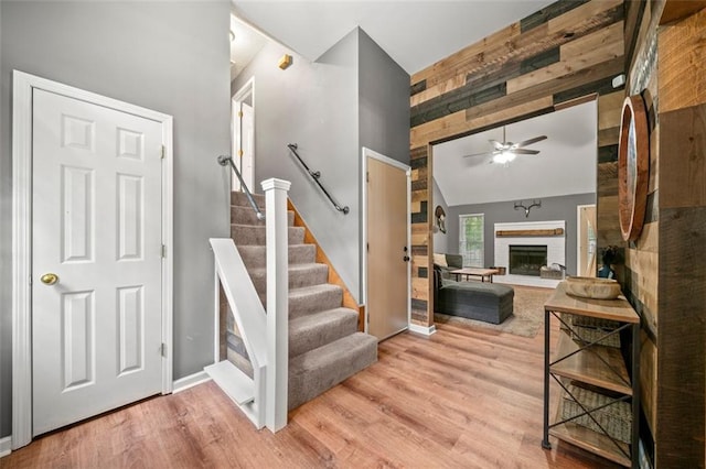 stairway featuring vaulted ceiling, ceiling fan, wood-type flooring, a fireplace, and wood walls