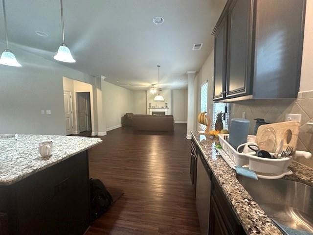 kitchen featuring decorative light fixtures, light stone countertops, dark wood-style floors, and a sink