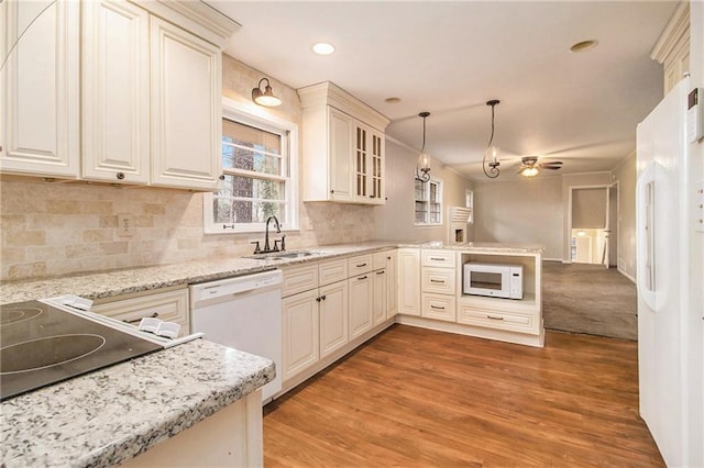 kitchen with kitchen peninsula, sink, white appliances, light stone counters, and pendant lighting