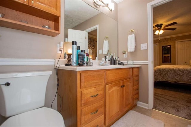 bathroom with ceiling fan, vanity with extensive cabinet space, crown molding, and toilet