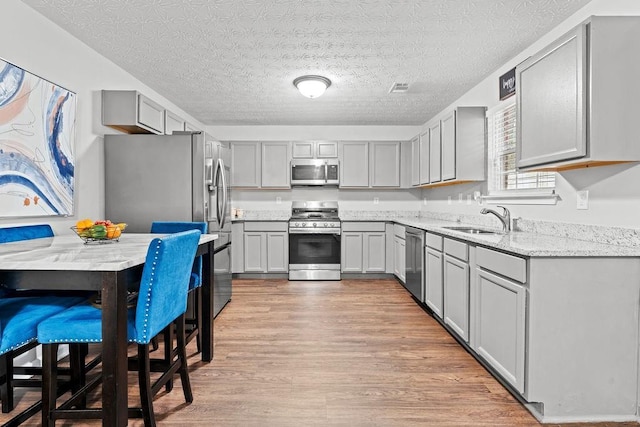 kitchen with sink, gray cabinetry, light hardwood / wood-style floors, stainless steel appliances, and light stone countertops