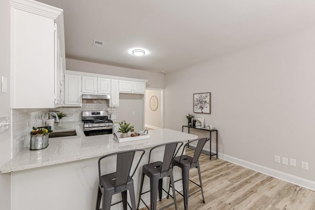 3329 Walt Stephens Rd, Stockbridge, GA 30281 - kitchen with stainless steel gas range, under cabinet range hood, a peninsula, decorative backsplash, and white cabinetry