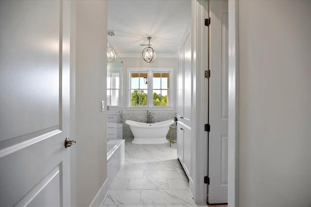 full bathroom with crown molding, marble finish floor, a soaking tub, and an inviting chandelier