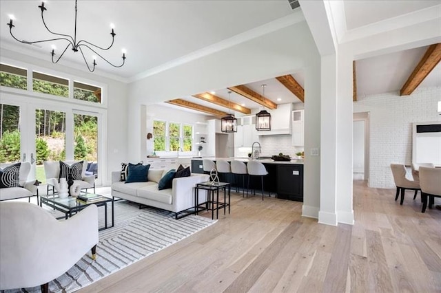 living room featuring ornamental molding, beamed ceiling, an inviting chandelier, french doors, and light wood-type flooring