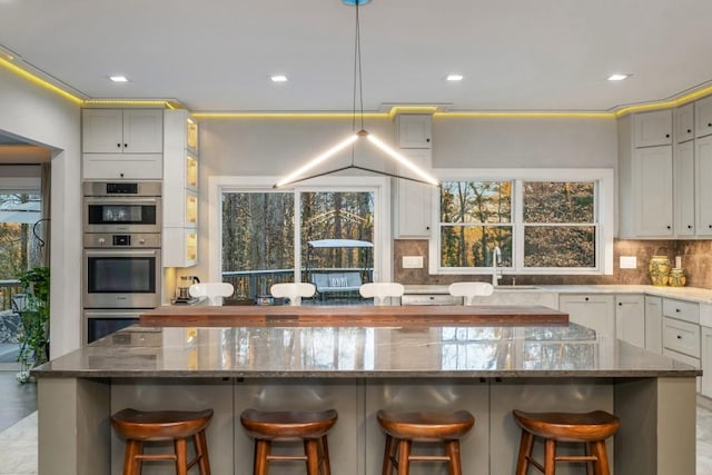 kitchen featuring dark stone countertops, stainless steel double oven, a breakfast bar area, and tasteful backsplash