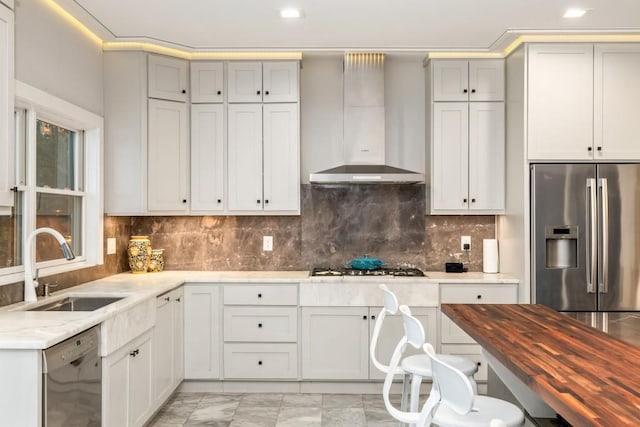 kitchen with appliances with stainless steel finishes, sink, white cabinetry, wall chimney exhaust hood, and decorative backsplash